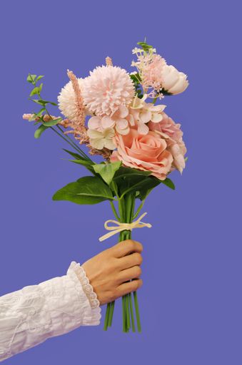 A vertical shot of a female hand holding a romantic bouquet made of pastel flowers