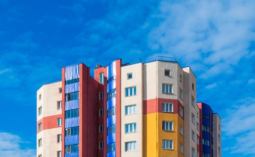 Modern multi-storey building with  multi-colored facade against blue cloudy clear sky.