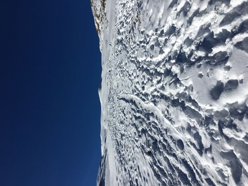 A vertical shot of the footsteps on the snow against the blue sky.