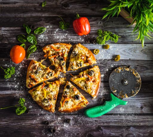 A top shot of a baked cut pizza and some on a wooden surface.