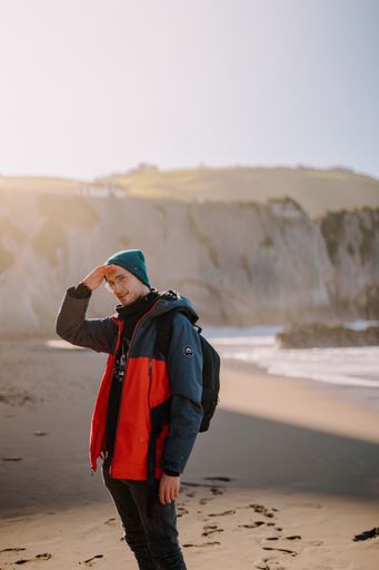 A vertical shot of a Hispanic guy in a coat standing on a beach.