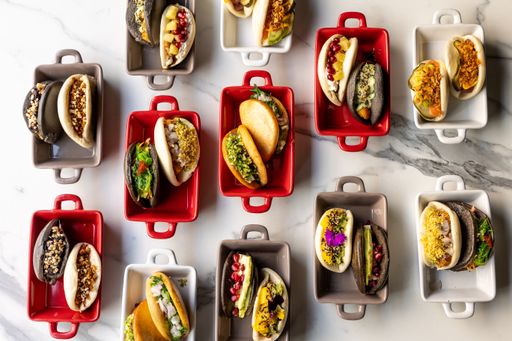 An overhead shot of colorful tacos with different foods placed in white red and gray cans on the table