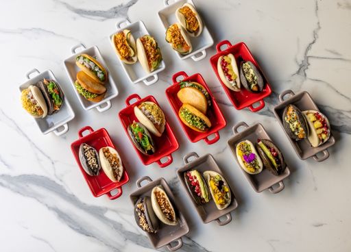 An overhead shot of tacos with different foods placed in white red and gray cans lined up on the table