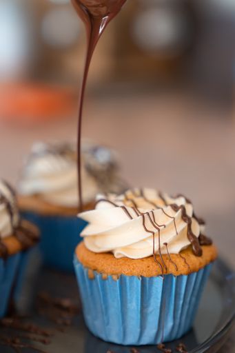 A vertical shot of cupcakes drizzled in chocolate with a blurry background