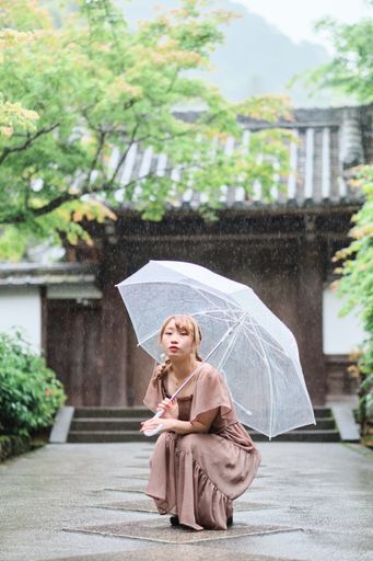 A Japanese girl squating on the ground under umbrella in rain