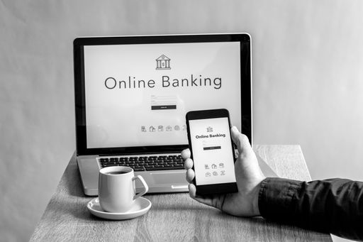 A grayscale of a phone and laptop with an online banking page on the display