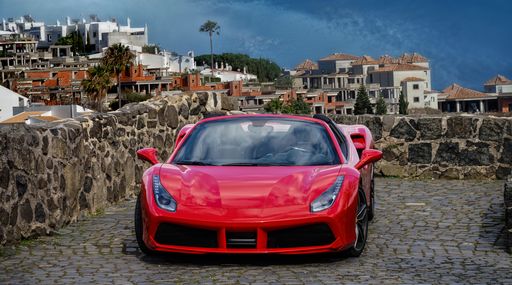 A beautiful red Ferrari 488 sportscar parked on the paved ground in a little town