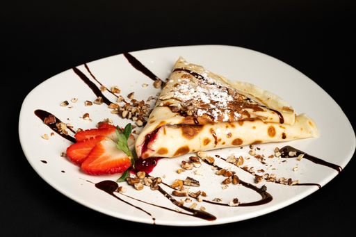 A closeup shot of the chocolate crepe with strawberry and walnuts on the white plate and the black background