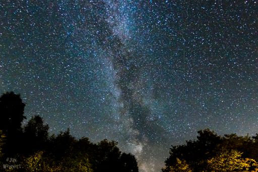 milky way over a typical swedish house in the forest illuminating the starry sky at night.