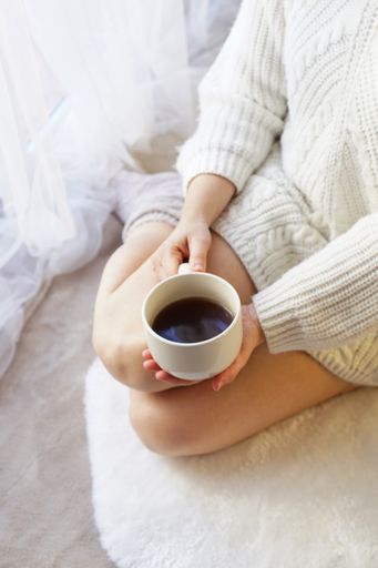 A vertical shot of a woman kneeling on the floor holding a white coffee cup