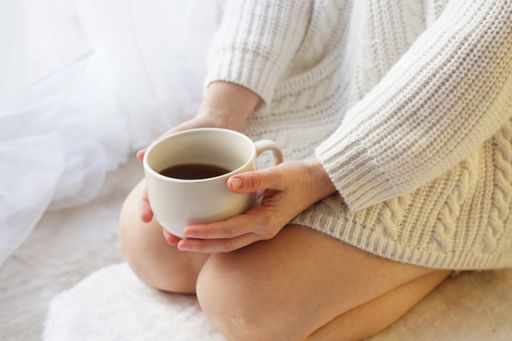 A shallow focus closeup of a woman kneeling on the floor holding a white cup