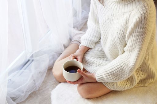 A high angle shot of a caucasian woman in a white sweater holding a white coffee cup