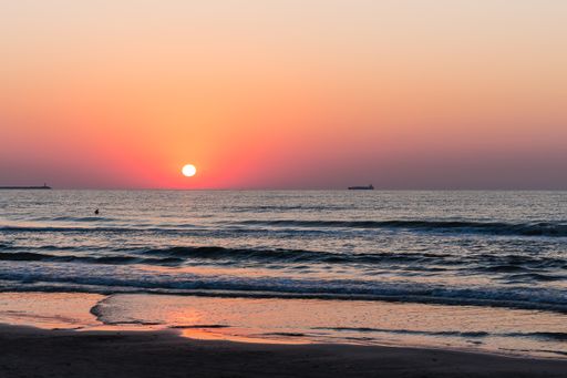 A mesmerizing view of the wavy ocean hitting the sandy beach and gleaming against the sunset
