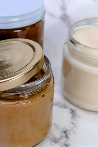 A vertical shot of three jars with lids filled with different types of creams and butters on the table