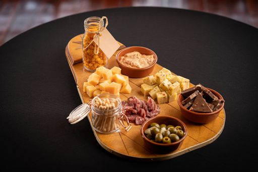 A closeup of a wooden trace with cheese assortment, green olives, chocolate bars, and other delicious food on a black surface