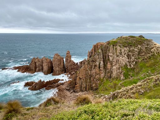 A scenic view of rocky cliffs surrounded by the ocean on cloudy sky backgroun