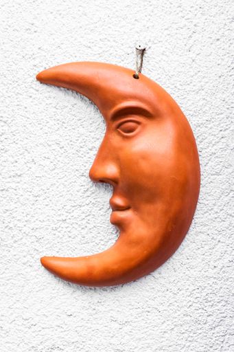 A vertical shot of a moon face statue hanging from a wall