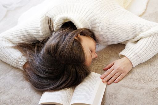 A woman with a warm sweater sleeping on the floor after reading a book at home