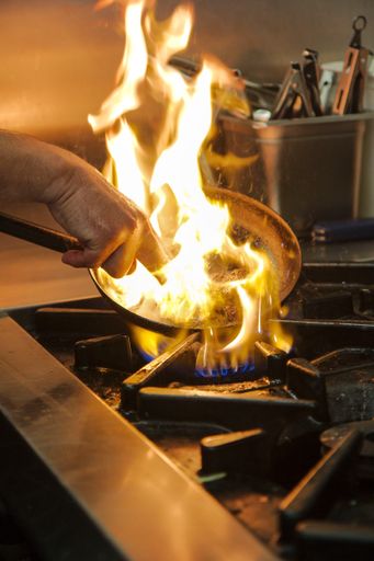 A professional chef using a pan to fry food in the kitchen with a flame bursting out on the oven
