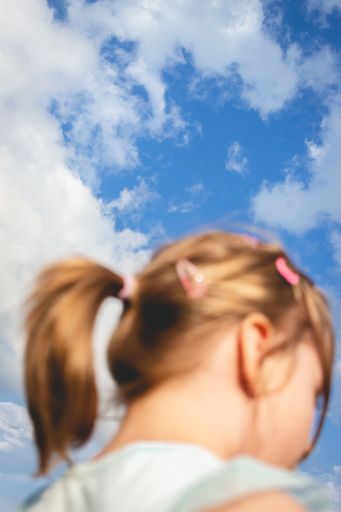 A vertical low angle shot of a girl with beautiful blue sky in frame