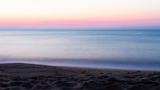 A beach surrounded by the sea with long exposure during the sunset in the evening