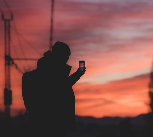 A silhouette shot of a male taking photos of the sunset