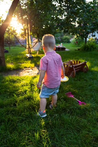 A back view of a cute blond baby boy playing in a grassy summer park