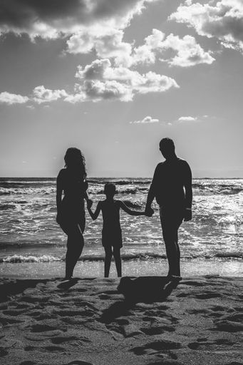 A vertical grayscale shot of a family silhouette standing with a beautiful seascape view behind