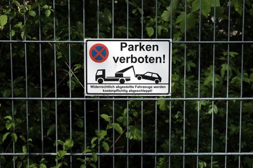 A metal white sign with "No Parking" written on it on the fence