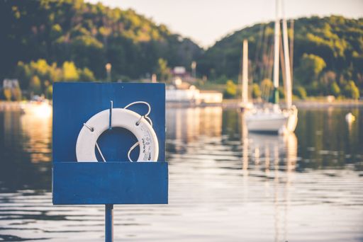 A selective shot of a white lifebuoy ring inside of a blue box on the background of a boats on the body of water