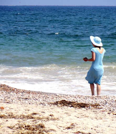 A vertical of a Caucasian female from behind with a blue dress walking on the beach