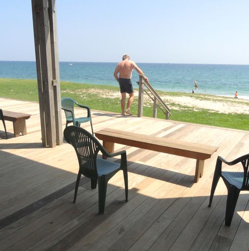 A Caucasian male going down the porch to the coastline covered with green grass against the seascape
