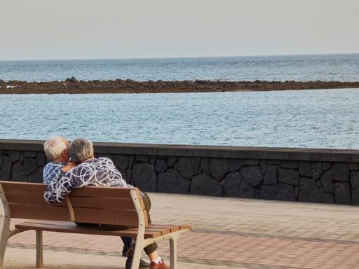 The elderly couple sitting on a bench in front of the sea.