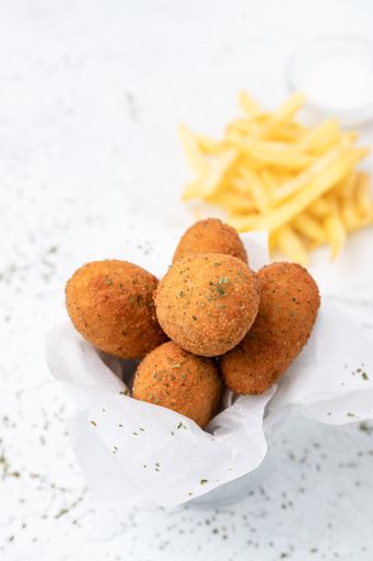 A closeup shot of fried balls and some fries on a white surface