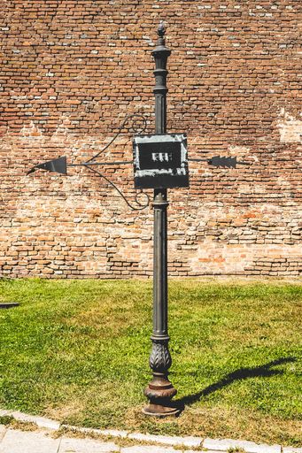 A vertical shot of a black sign with an arrow against a brick wall