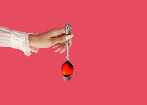A female's hand holding a vintage spoon with a red heart on a pink background with copyspace - the concept of growing love on Valentine's Day