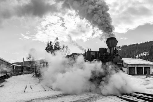 A grayscale shot of an old vintage stream train with heavy smoke against a cloudy sky