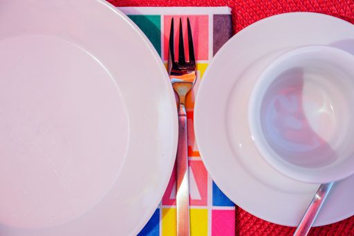 An overhead closeup shot of a plate and a cup with a fork on a red surface
