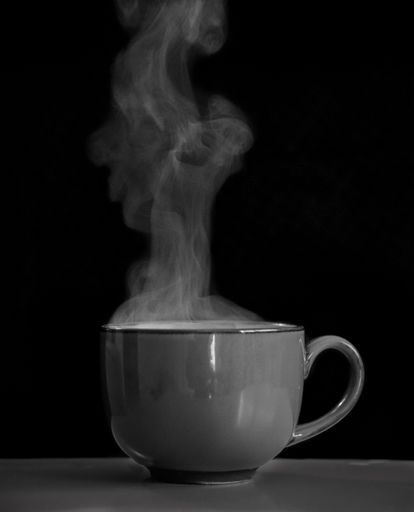 A black and white closeup of a coffee cup with steam coming out of it