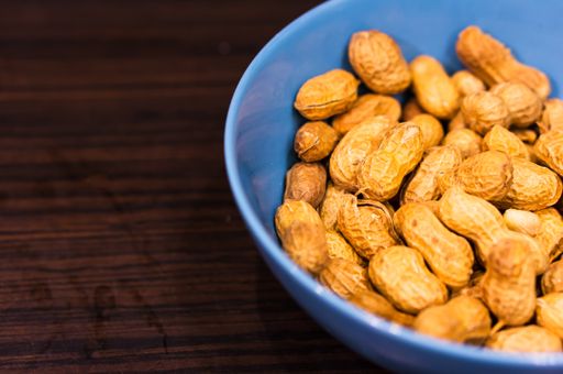 A selective focus shot of a vibrant blue bowl of peanuts on a  dark brown table