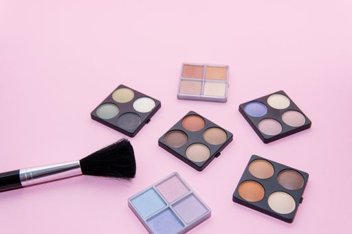 Make-up set with various colors and a brush on pink background. Beauty concept, copy spac