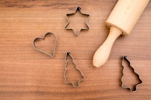A flat lay of Christmas cookie cutters and rolling pin on wooden surface