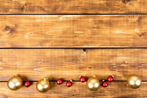 A flat lay of red and gold Christmas ornaments on a wooden background with copy space