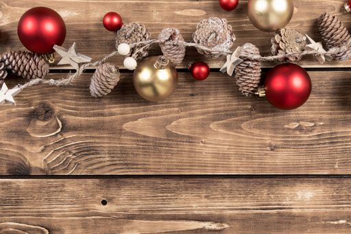 A flat lay of Christmas string decor with red and gold baubles and pine cones on a wooden background with copy space