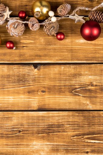 A flat lay of Christmas string decor with red and gold baubles and pine cones on a wooden background with copy space