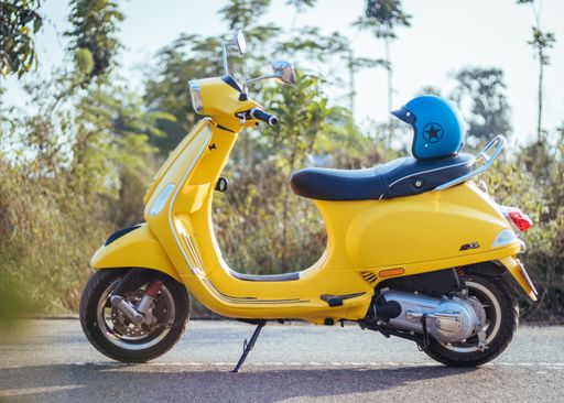 A closeup view of a beautiful yellow Vespa SXL 125 with a blue helmet in a street