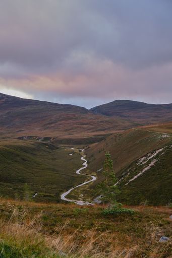 a beautiful view of a mountain river between hills under overcast sky at sunset in Scotland