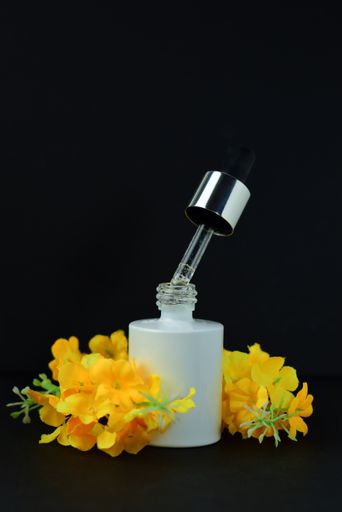 A vertical shot of the cosmetic dropper container and decorative yellow flowers underneath it on the black background