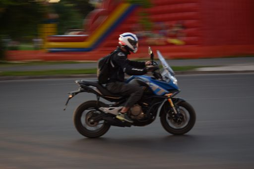 A person riding a motorcycle in the street with a children's trampoline in the background