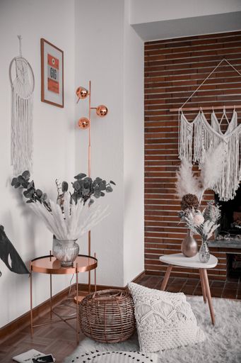 A vertical shot of a cozy interior with a woven pillow, dream catcher, and a macrame cord on the wall